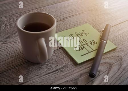 Immagine ravvicinata della nota con il testo "ma prima, caffè" e una tazza di caffè. Foto Stock