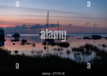 All'alba sul Tamigi a Leigh on Sea, Essex, Regno Unito, con il cielo rosso riflesso nelle acque piane e calme. Yacht e barche sagomati Foto Stock