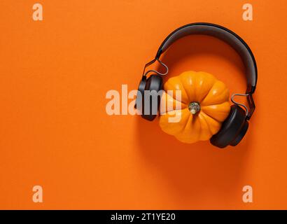 Concetto di festa di Halloween. Zucca autunnale con cuffie wireless nere su sfondo arancione con spazio per la copia. Foto Stock