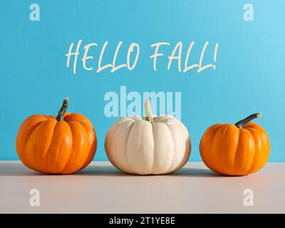 Zucche crude autunnali su tavolo da cucina in legno su sfondo blu con messaggio Hello Fall. Foto Stock