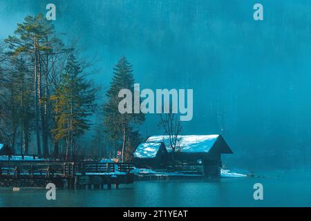 Bohinj Lake Boathouse sul lungomare nella nebbiosa mattinata invernale con cabine e moli in legno, attenzione selettiva Foto Stock