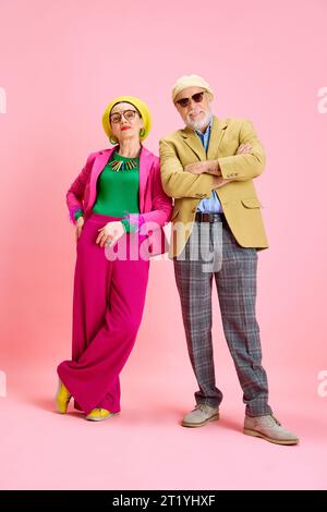 Elegante coppia anziana, bell'uomo e bella donna con abiti eleganti che si posano sullo sfondo rosa dello studio Foto Stock