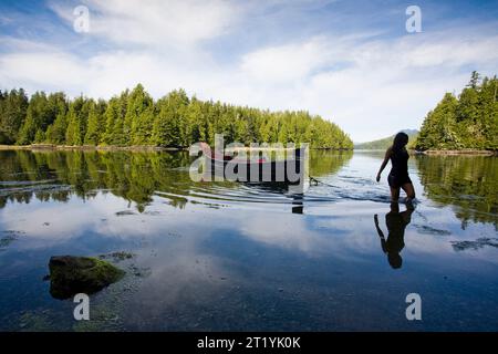 Una donna che si staglia contro un cielo azzurro si getta in una piccola insenatura vicino a Tofino. Foto Stock