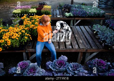 Una donna che indossa un cappotto arancione lavora nella sua serra urbana in un grande asilo. Foto Stock