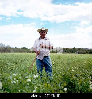 Un ritratto di un contadino in piedi in un campo che indossa un cappello da cowboy e tiene una pala. Foto Stock