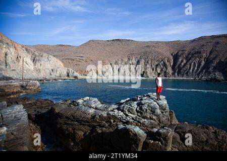 Un giovane si trova su uno sperone roccioso vicino a una piccola baia vicino a Pescadero, Baja California Sur, Messico. Foto Stock