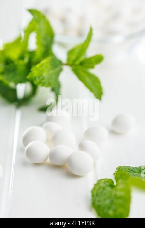 Caramelle alla menta. Ossa di mentolo e foglie di menta sul tavolo bianco. Foto Stock