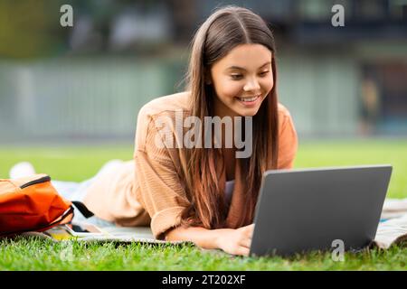 Studentessa felice immersa nel lavoro con notebook, campus universitario tranquillo Foto Stock