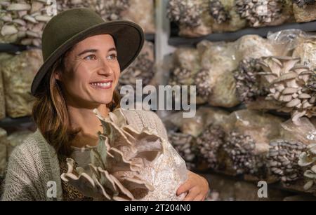 Giovane donna sorridente che tiene un terreno coltivato con funghi ostriche Foto Stock