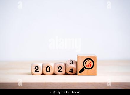 2024 felice anno nuovo con nuovi concetti di tendenze aziendali. Capovolgere il calendario 2023-2024 anni e la lente di ingrandimento con icona grafico della crescita su legno grande Foto Stock