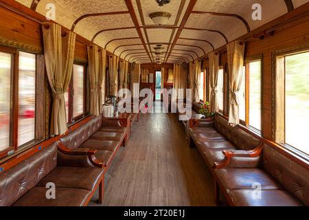 Interno di una vecchia carrozza ferroviaria d'epoca con sedia in pelle, pavimento in legno, tende gialle Foto Stock