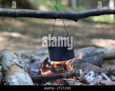 Bollitore turistico affumicato sopra la fiamma del fuoco da campeggio nella foresta Foto Stock