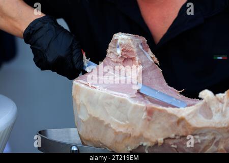 Primo piano delle mani di un cameriere esperto mentre si affetta il tipico prosciutto cotto Triestino Foto Stock