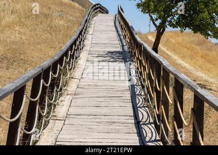 Ponte di recinzione in legno sul prato e sull'erba. Fatto di funi. Percorso del marciapiede Foto Stock