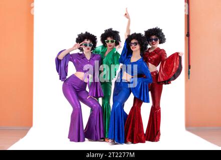 Un gruppo di ragazze con abiti svasati colorati e parrucche afro posa in uno studio fotografico. Stile discoteca degli anni '80 o '70. Foto Stock