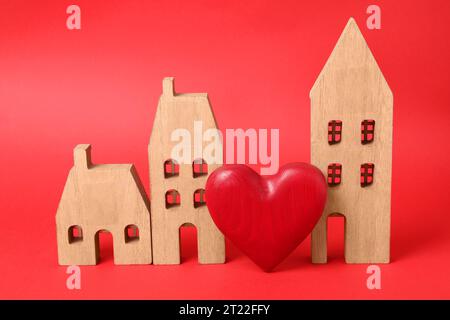 Concetto di relazione a distanza. Modelli di casa in legno e cuore decorativo su sfondo rosso Foto Stock