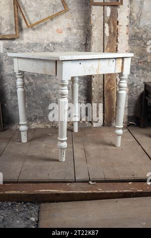 Stile vintage. Vecchio tavolo rotto difettoso in una vecchia camera sporca con altre cose d'epoca Foto Stock