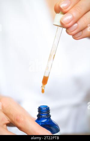 Un'iniezione laterale ravvicinata di una bottiglia blu con siero, gocce che cadono da una pipetta. Primo piano di gocce di siero idratante per la pelle. Un prodotto per midd Foto Stock