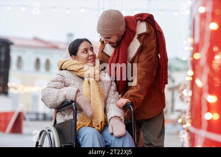 Ritratto di una coppia romantica con una donna in sedia a rotelle che si gode di un appuntamento all'aperto nel mercatino di Natale Foto Stock