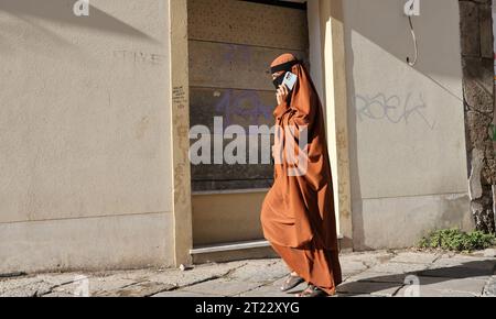 Una donna musulmana usa il suo smartphone mentre cammina attraverso la città vecchia di Palermo in Sicilia, Italia Foto Stock