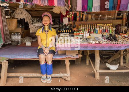 Karen Woman di Pai a Mae Hong Son, Thailandia, con anelli in ottone, siede su un'altalena di legno in un villaggio rustico e indossa un abito Karen dai colori vivaci Foto Stock