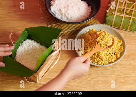 Processo di riempimento dello stampo di banh chung con fagioli mung durante la preparazione della torta quadrata per le vacanze vietnamite Foto Stock