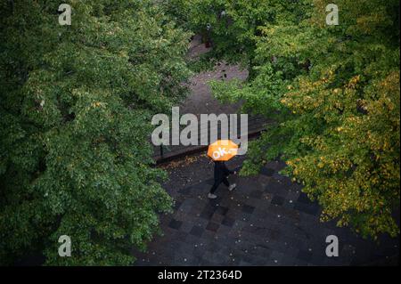 07.10.2023, Berlino, Germania, Europa - persona che tiene un ombrello cammina lungo una strada bagnata in un giorno di pioggia autunnale nel quartiere berlinese di Charlottenburg. Foto Stock