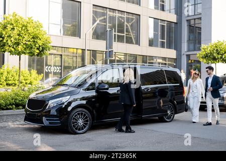 Autista donna attende un viaggiatore d'affari vicino al minivan taxi Foto Stock