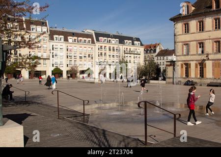 Francia, Fontainebleau, Place de la République: I bambini giocano tra i beccucci d'acqua in una giornata di sole in primavera. Foto Stock