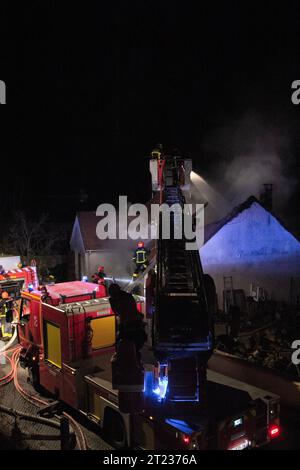 Il pompiere assiste a un incendio di notte in un villaggio in Francia con le macchine antincendio e una scala aerea. Foto Stock