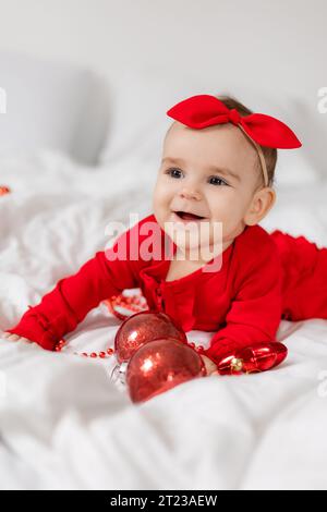 Carino e felice bambino con una tuta rossa è sdraiato sullo stomaco a letto Foto Stock