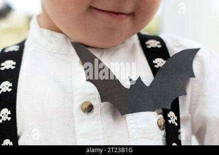 Concetto di Halloween. Vacanze autunnali. Bambino, niente faccia. Nella tasca di una camicia bianca si trova un pipistrello di carta nera. Ritratto. Primo piano. Messa a fuoco morbida. Foto Stock