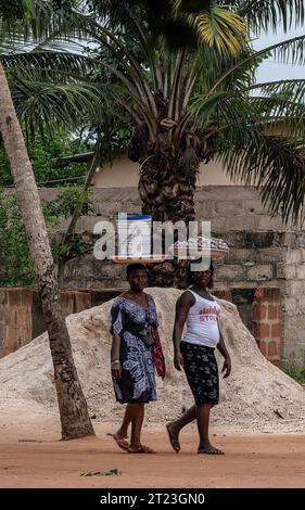 Lomé, Togo - 14 maggio 2023. Due donne camminano attraverso un villaggio del Togo mentre trasportano pacchi sulla testa nel modo tradizionale Foto Stock