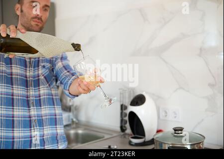 Dettagli sulla bottiglia di vino nelle mani di un bel giovane uomo caucasico barbuto che versa il vino in un bicchiere da una bottiglia, in piedi a casa Foto Stock
