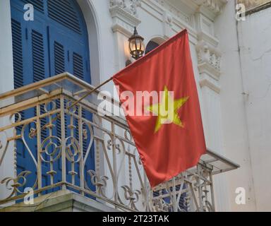 Bandiera nazionale rossa d'oro del Vietnam che sventola con orgoglio dal balcone di una casa nello stile coloniale francese del quartiere vecchio di Hanoi Foto Stock