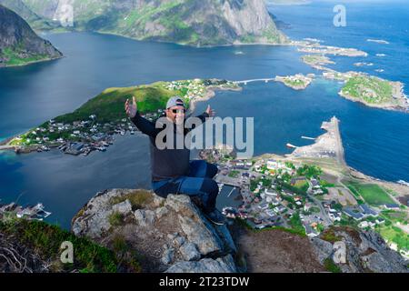 Rilassato e felice escursionista gode di una vista mozzafiato sulle cime di Reinebringen delle isole Lofoten, dei fiordi e della Norvegia Foto Stock