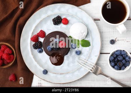 Delizioso fondente di cioccolato servito con frutti di bosco freschi e gelato su un tavolo di legno bianco, piatto Foto Stock