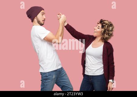 Ritratto di una donna positiva sorridente e sorpreso un uomo scioccato che si tiene per mano e si guarda l'un l'altro con emozioni diverse. Riprese in studio per interni isolate su sfondo rosa. Foto Stock