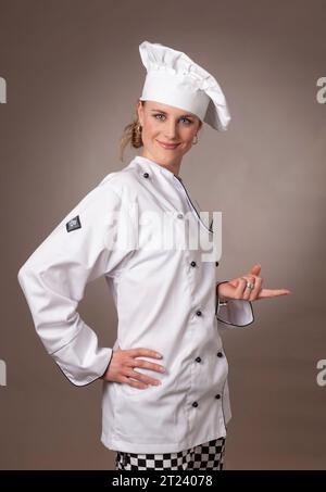 Attraente chef donna in bianco, che sembra bilanciare un oggetto Foto Stock