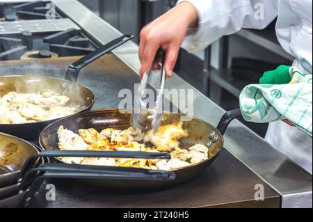 Chef sfocati cucinano il cibo in padelle in un ristorante commerciale o nella cucina di un hotel Foto Stock