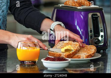 Persona che prepara il pane tostato per colazione con succo d'arancia, burro e spalmare Foto Stock