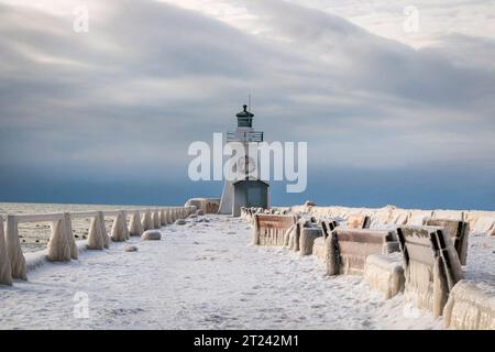 Formazioni di ghiaccio spesse sulle barre di protezione del molo. E panchine, paesaggio invernale sul lago con faro e cielo tempestoso, paese delle meraviglie invernali Foto Stock