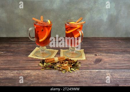 Due bicchieri di vino rosso caldo su tovaglioli con fette di arancia e mela su un tavolo di legno, accanto a una manciata di spezie secche. Primo piano. Foto Stock