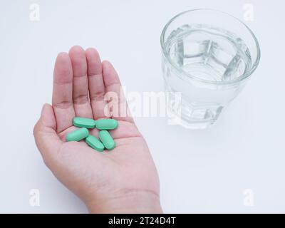 Mano che tiene pillole mediche verdi e un bicchiere d'acqua su sfondo bianco. concetto di salute Foto Stock