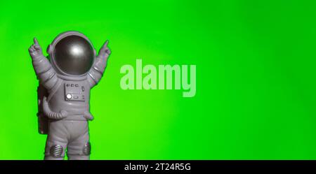 Astronauta giocattolo di plastica su sfondo chiave chroma verde Template Mock up Copy space. Concetto di viaggio fuori terra, voli commerciali privati spaziali. Missioni spaziali e Sostenibilità Foto Stock