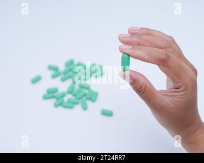 Mano che tiene pillole mediche verdi su sfondo bianco Foto Stock