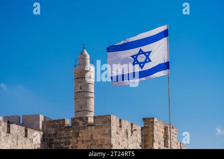 La bandiera di Israele ondeggia sul cielo blu con la Torre di Davide sullo sfondo sfocata Foto Stock