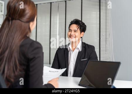Candidato di lavoro maschile asiatico reclutato da una giovane donna d'affari adulta datore di lavoro sulla scrivania nell'ufficio aziendale mentre ha con sé un computer portatile. Concetto di reclutamento professionale Foto Stock