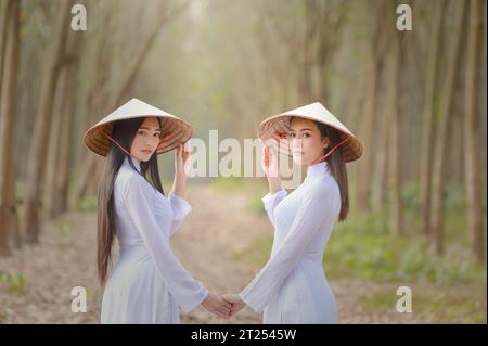 Ritratto di due donne asiatiche in abiti tradizionali in piedi in una foresta che si tiene per mano, Vietnam Foto Stock