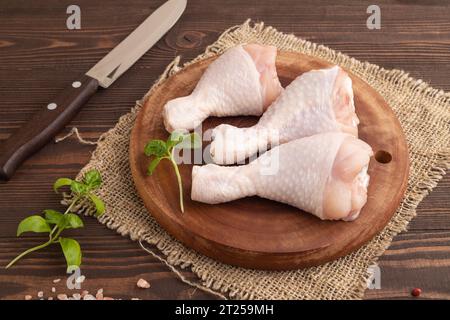Cosce di pollo crude con erbe e spezie su un tagliere di legno su fondo di legno marrone e tessuto di lino. Vista laterale, primo piano Foto Stock